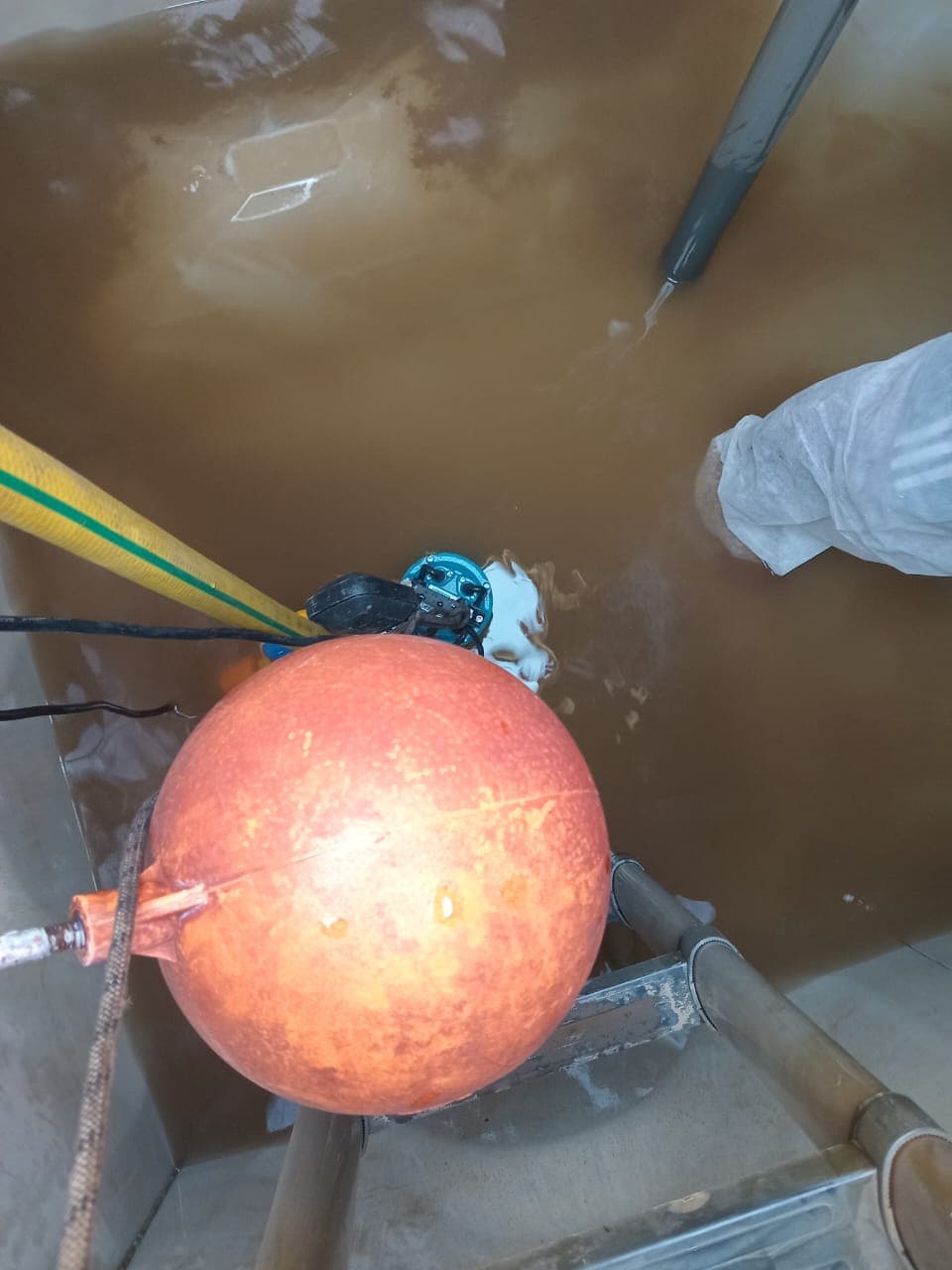 Second angle of tank before cleaning — murky brown water level, technician in full PPE entering for pre-clean assessment