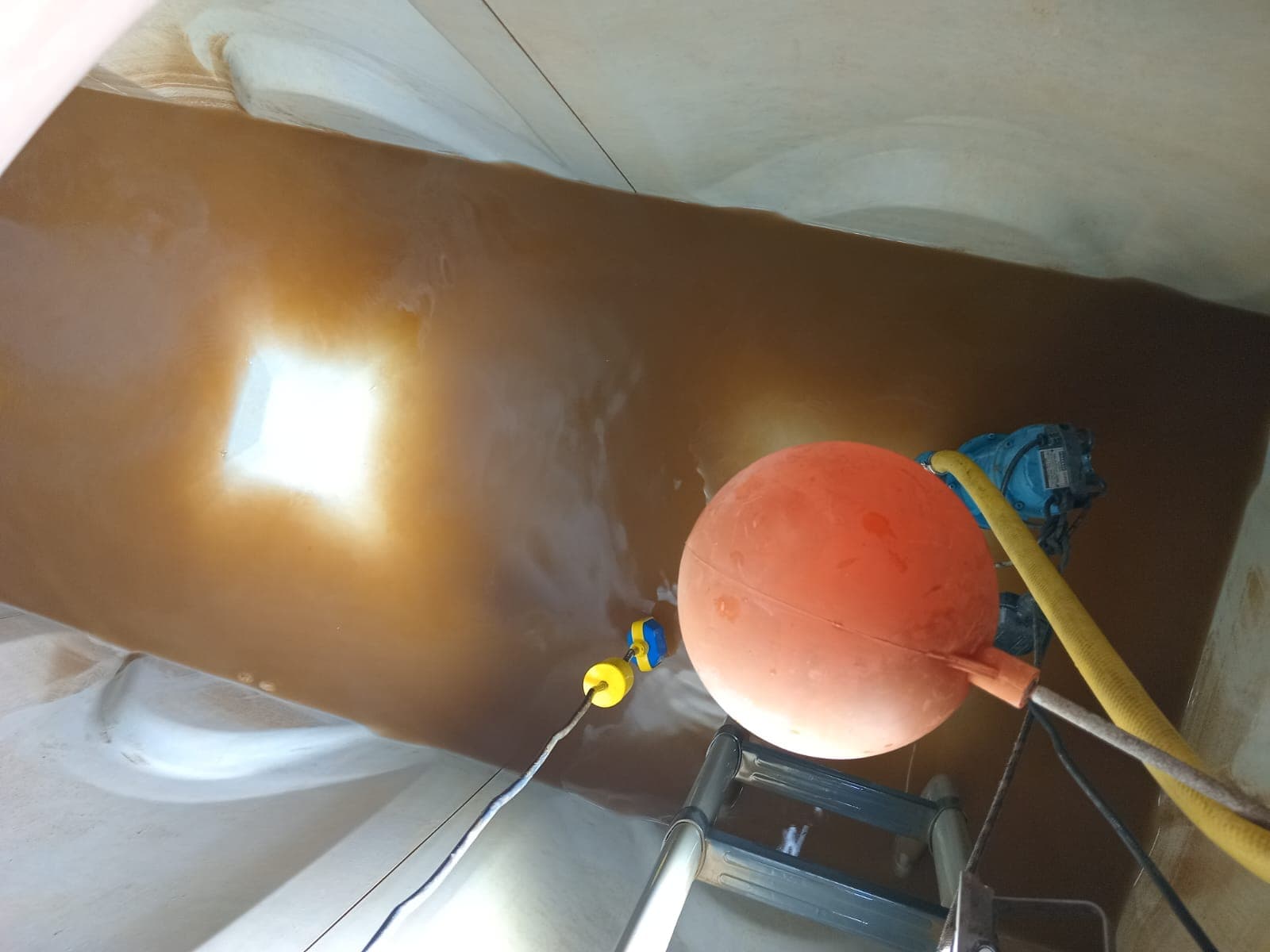 Main tank interior before cleaning — brown sediment-laden water, visible contamination across the entire tank floor